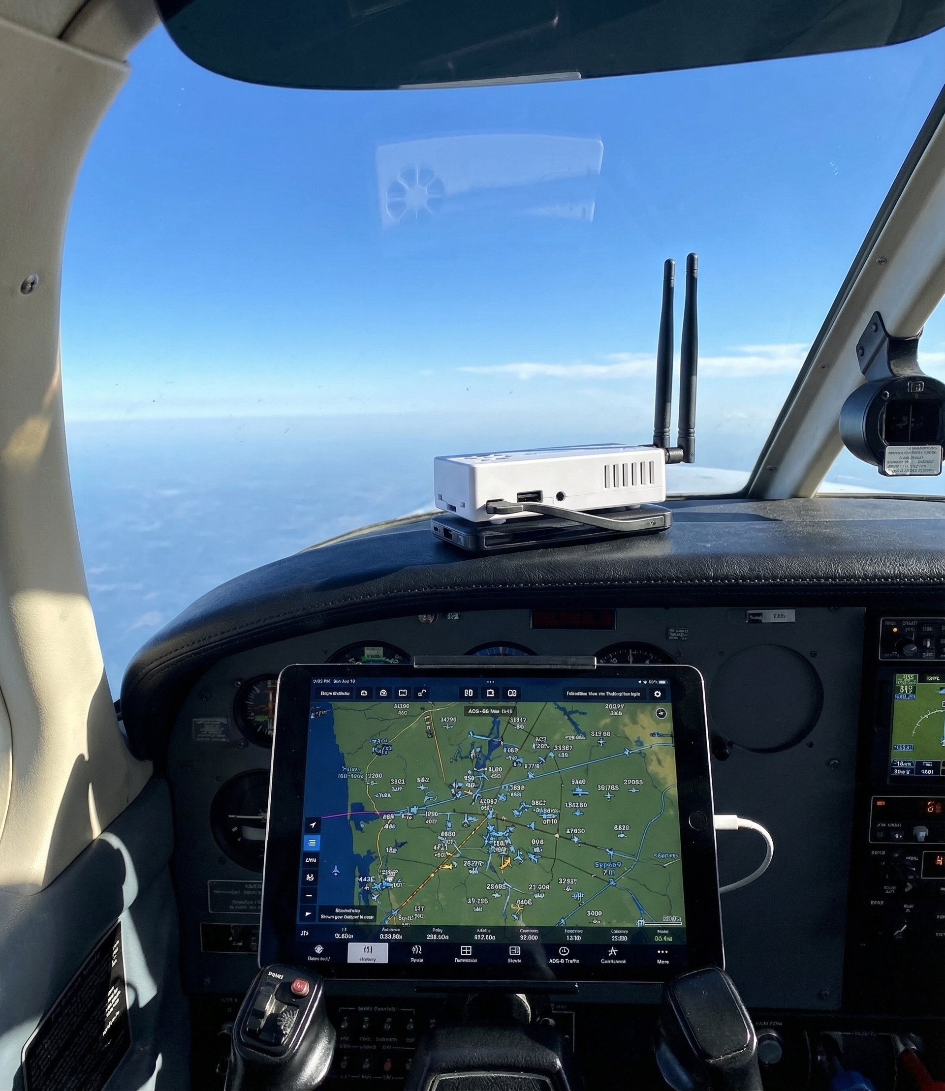 Stratux ADS-B receiver on cockpit glareshield with iPad showing ADS-B traffic map, blue sky through windshield
